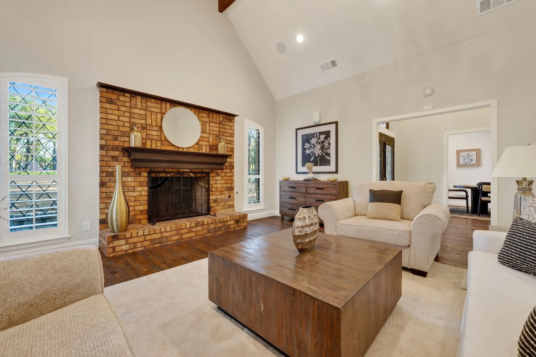 Vaulted ceiling with exposed beam, brick fireplace with wood mantel, wood-finish flooring, white wall paint, and white trim throughout