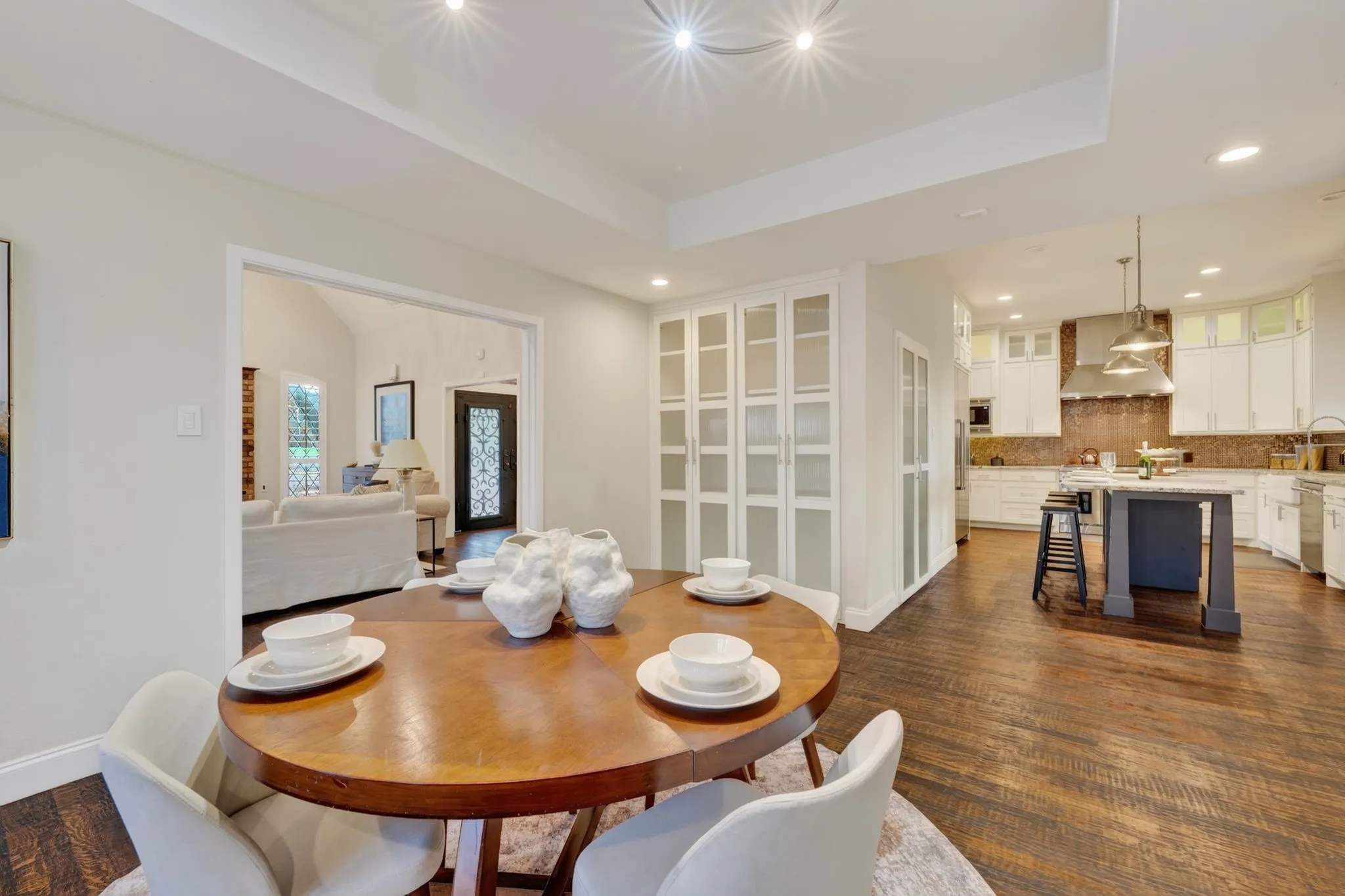 Recessed lighting, wood flooring, white built-in cabinetry, kitchen island with seating, and stainless steel range hood
