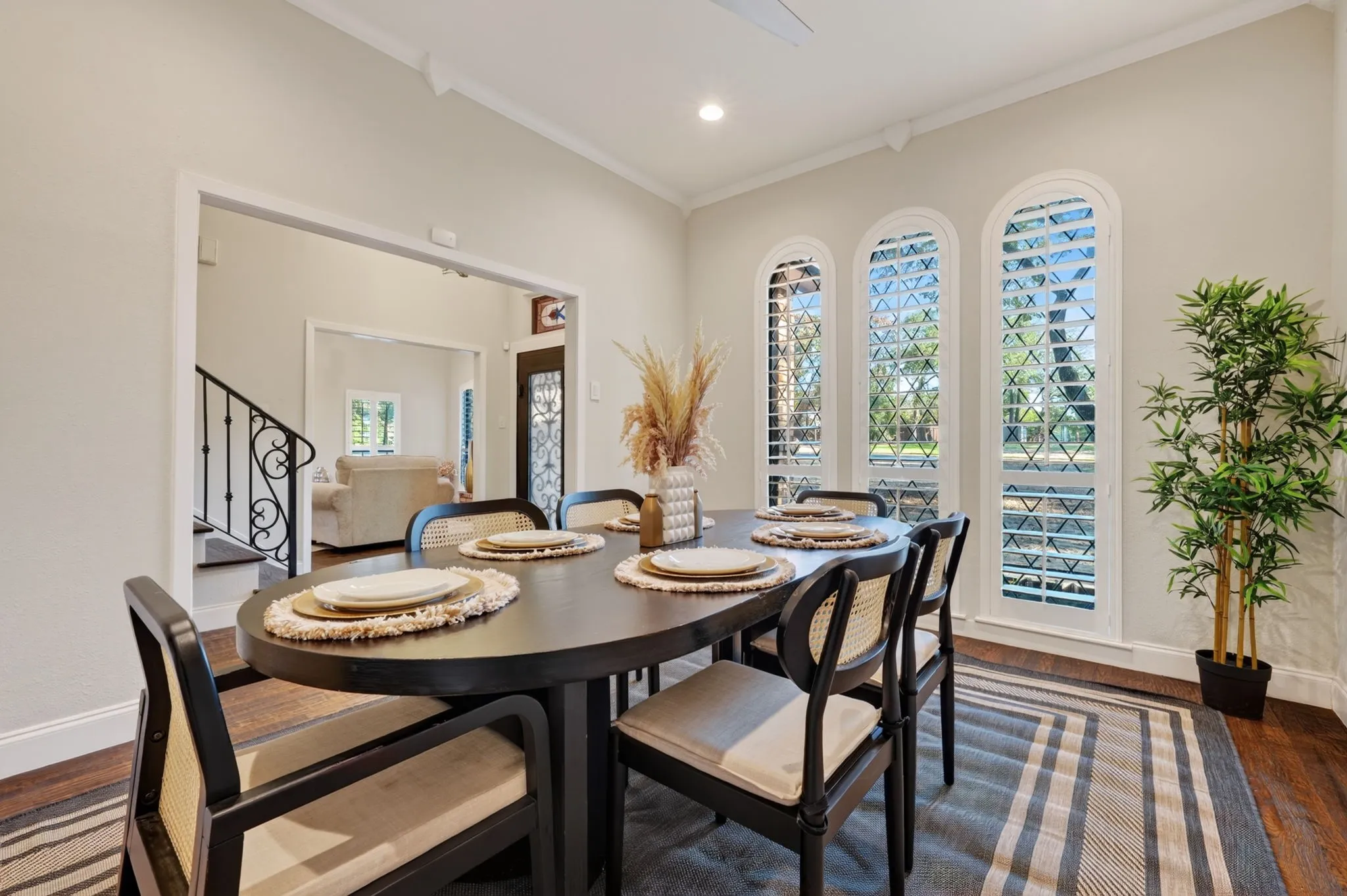 Dining area featuring three arched windows with plantation shutters, wood flooring, and crown molding