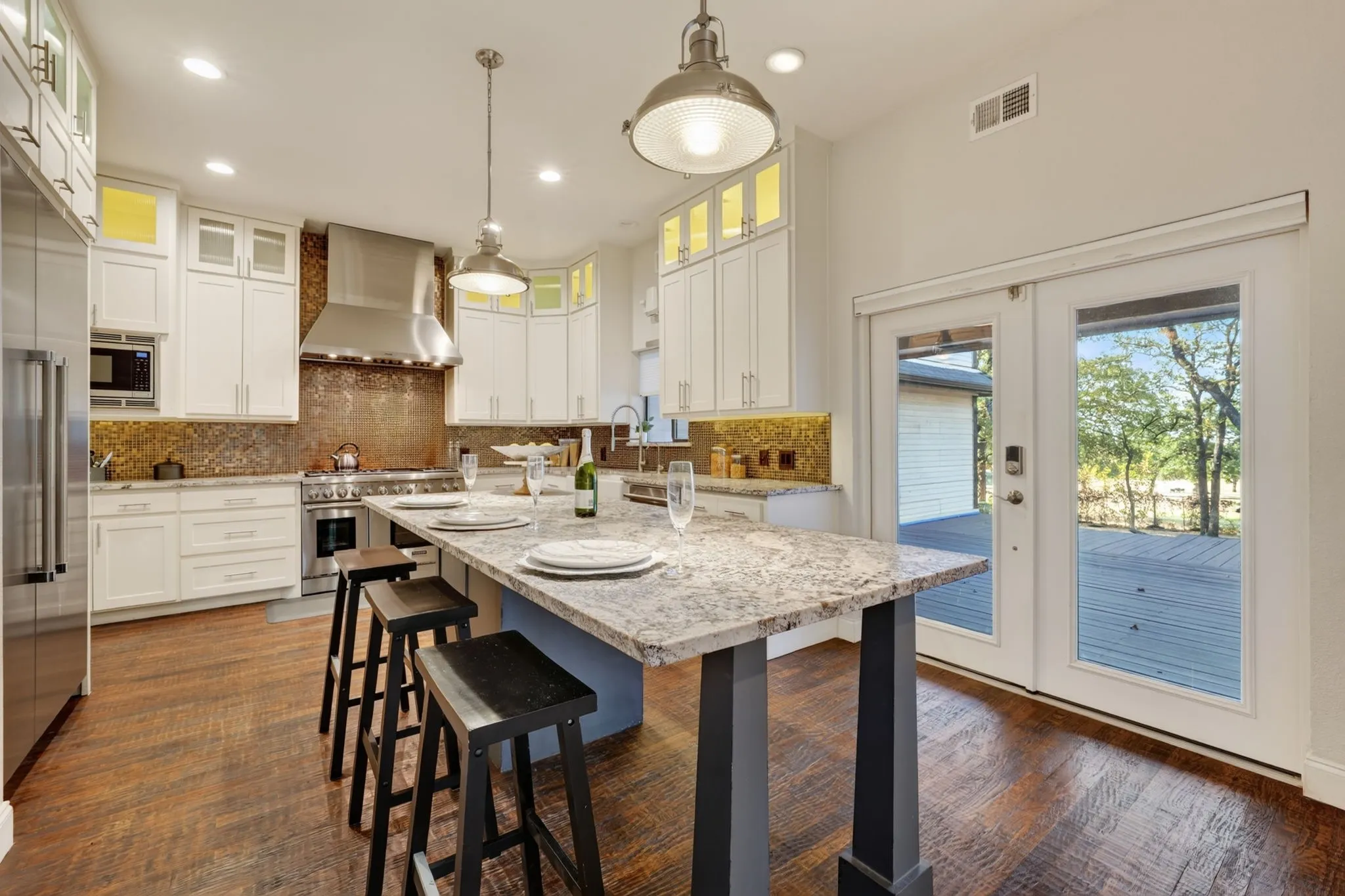 Kitchen featuring an expansive island with a light-toned countertop, wood flooring, white cabinetry, stainless steel appliances, and a full-height tile backsplash