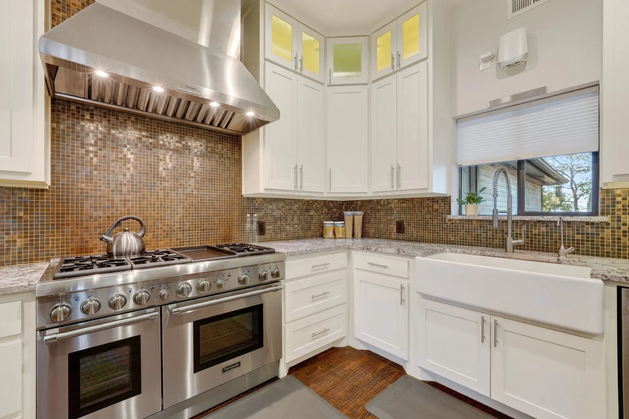 Stainless steel professional-grade range, coordinating range hood, mosaic tile backsplash, farmhouse-style sink, and light-toned cabinetry