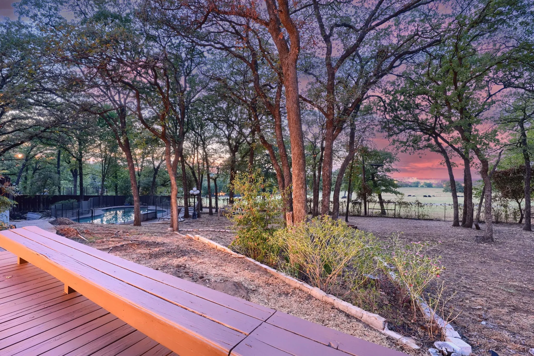 Wood-finish deck with built-in bench seating, surrounded by mature trees, and a visible swimming pool