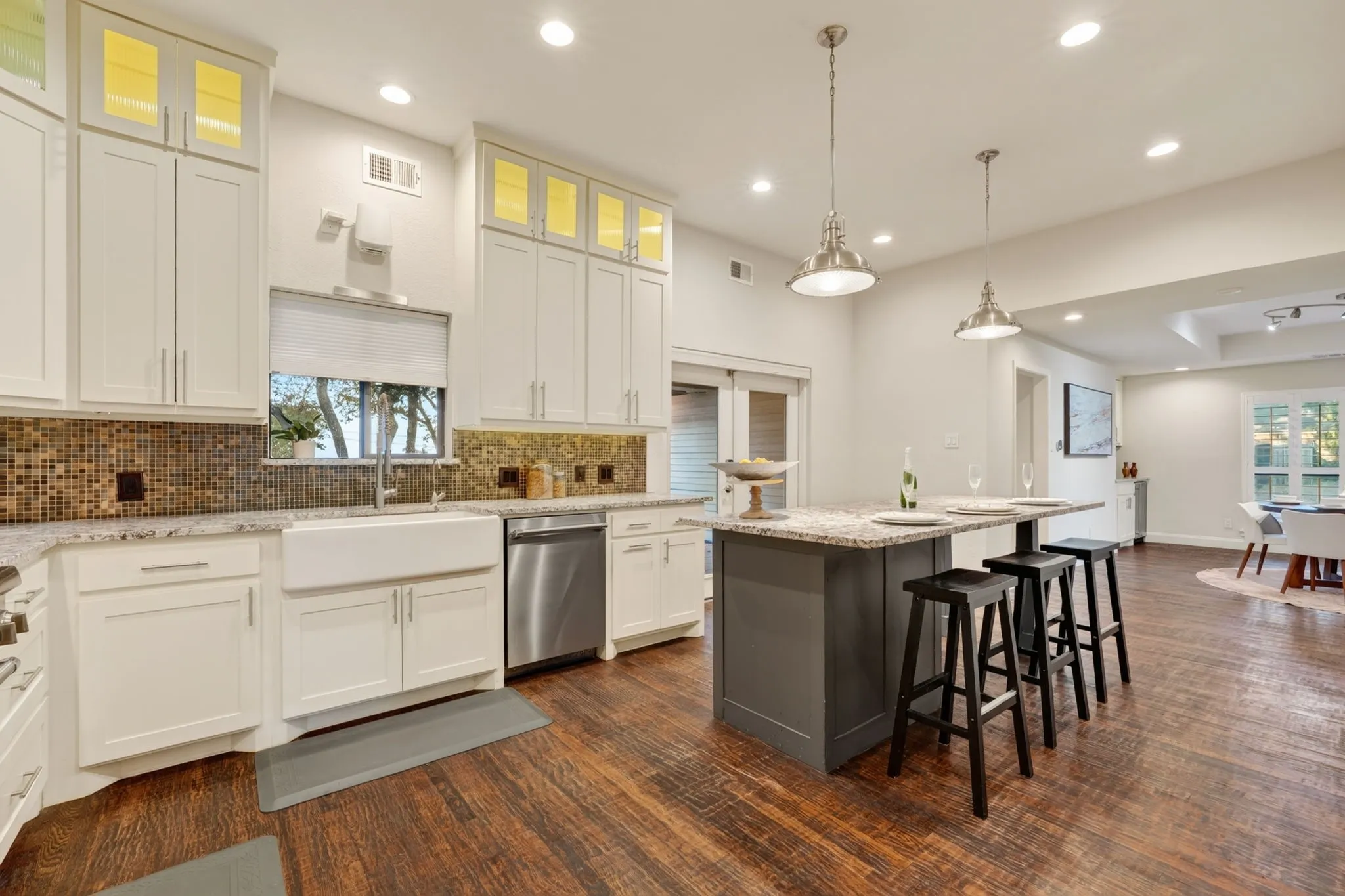 Spacious kitchen featuring white cabinetry, a mosaic tile backsplash, stainless steel appliances, a farmhouse sink, and wood flooring
