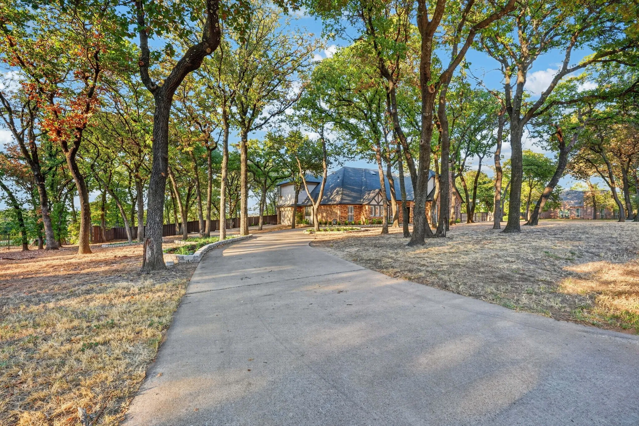 Entry with a concrete drive, surrounded by mature trees, leading to a brick and timber-frame exterior residence with a dark-pitched roof. Side entry 2 car garage