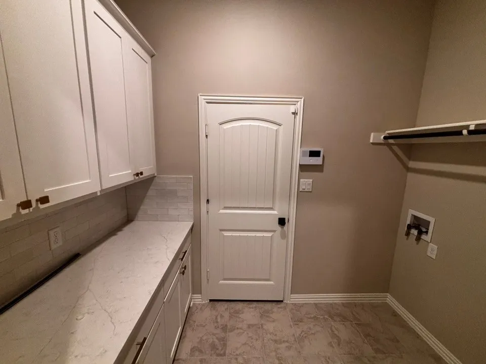 Laundry area featuring white shaker-style cabinetry, a light-toned countertop, and a tiled backsplash