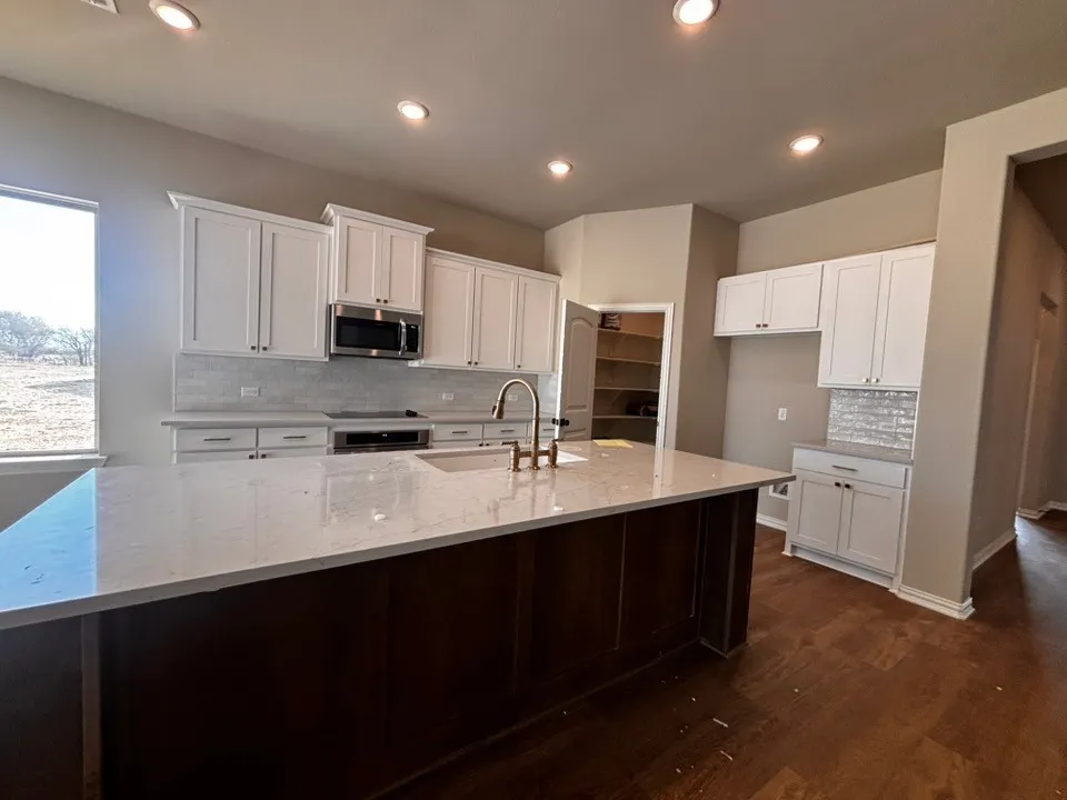 Kitchen featuring a center island with a light-toned countertop, white cabinetry with dark hardware, stainless steel microwave, dark wood-finish flooring, and a walk-in pantry