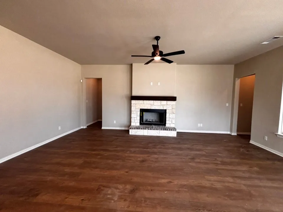 Expansive room featuring wood-finish flooring, a stone-clad fireplace with a wood mantle, and a ceiling fan