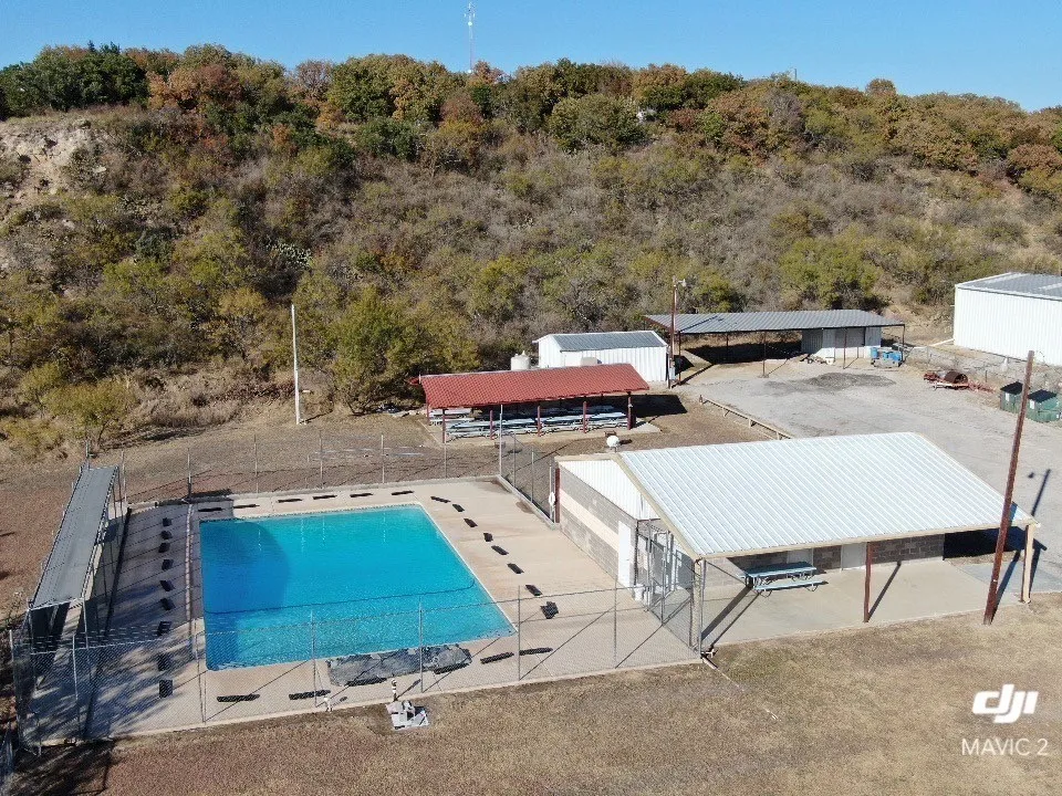 Outdoor swimming pool with a surrounding fence, covered picnic area, and an additional covered structure