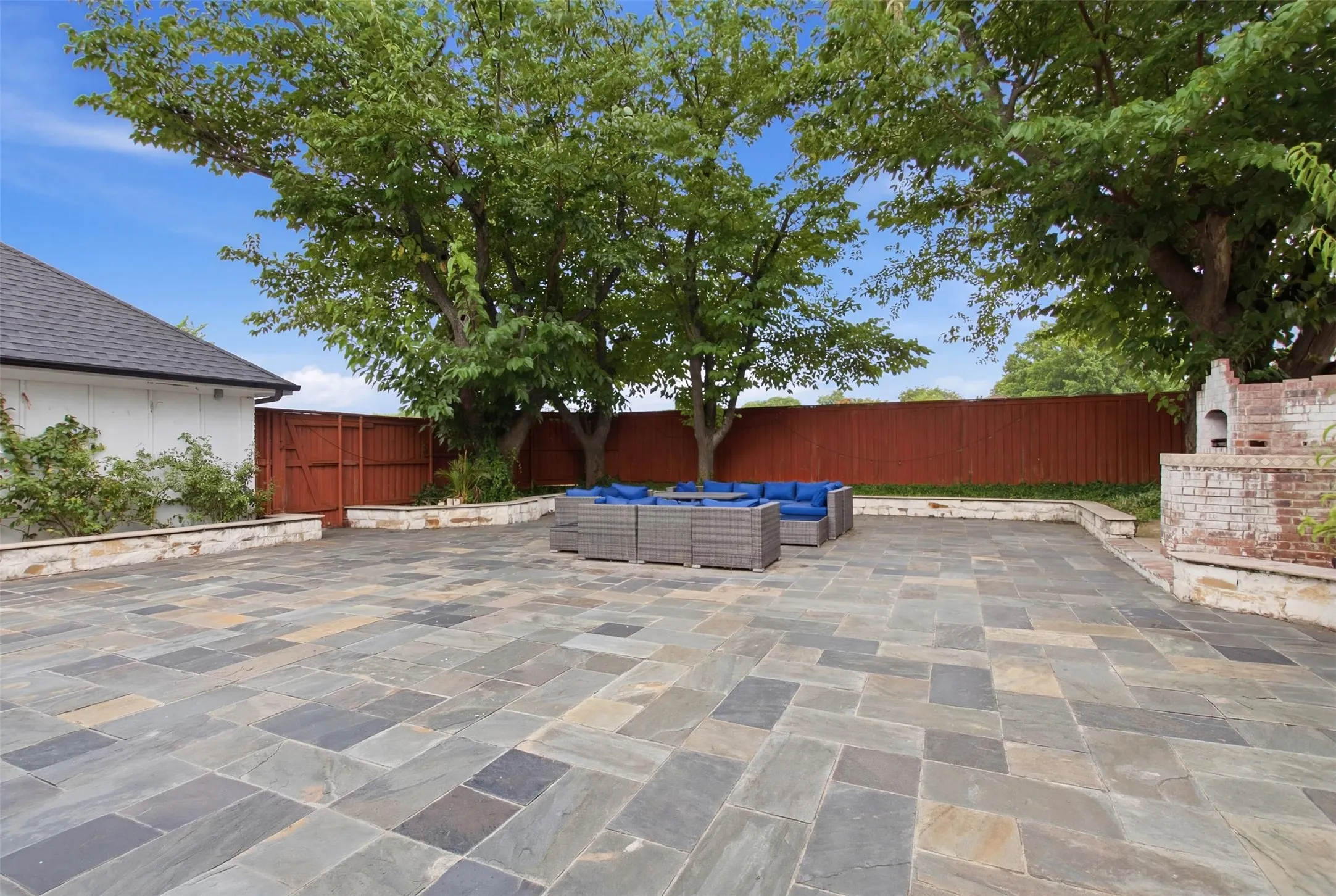 Expansive outdoor patio featuring multi-toned flagstone paving, a perimeter stone retaining wall, and a built-in brick outdoor fireplace