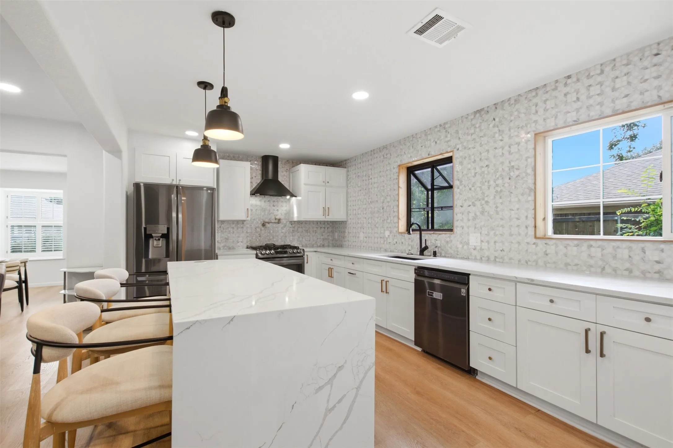 Open-concept kitchen featuring a waterfall island with a quartz countertop, white shaker cabinetry, stainless steel appliances, and wood-finish flooring