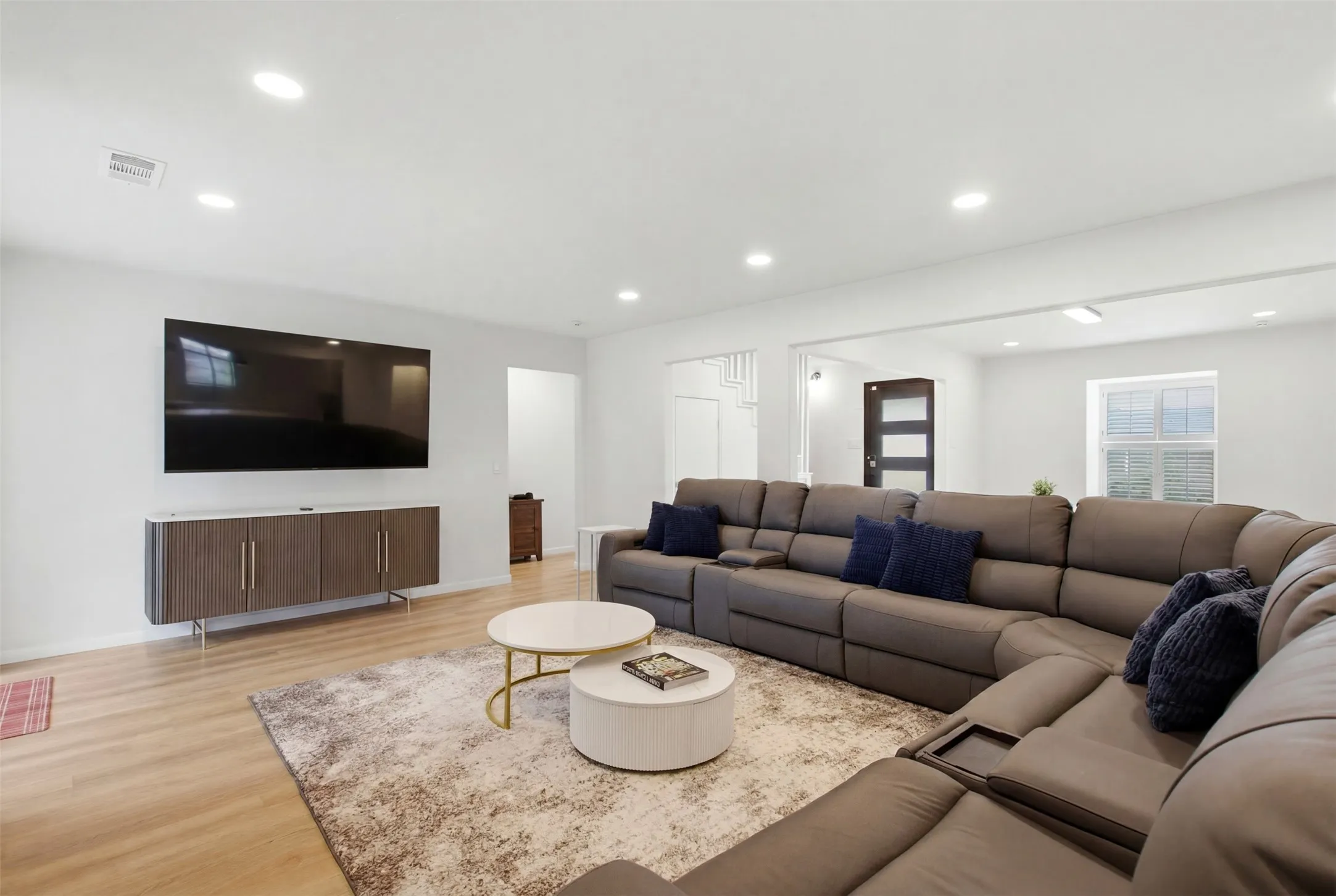 Bright living area featuring wood-finish flooring, recessed lighting, and a mounted media console with a white countertop