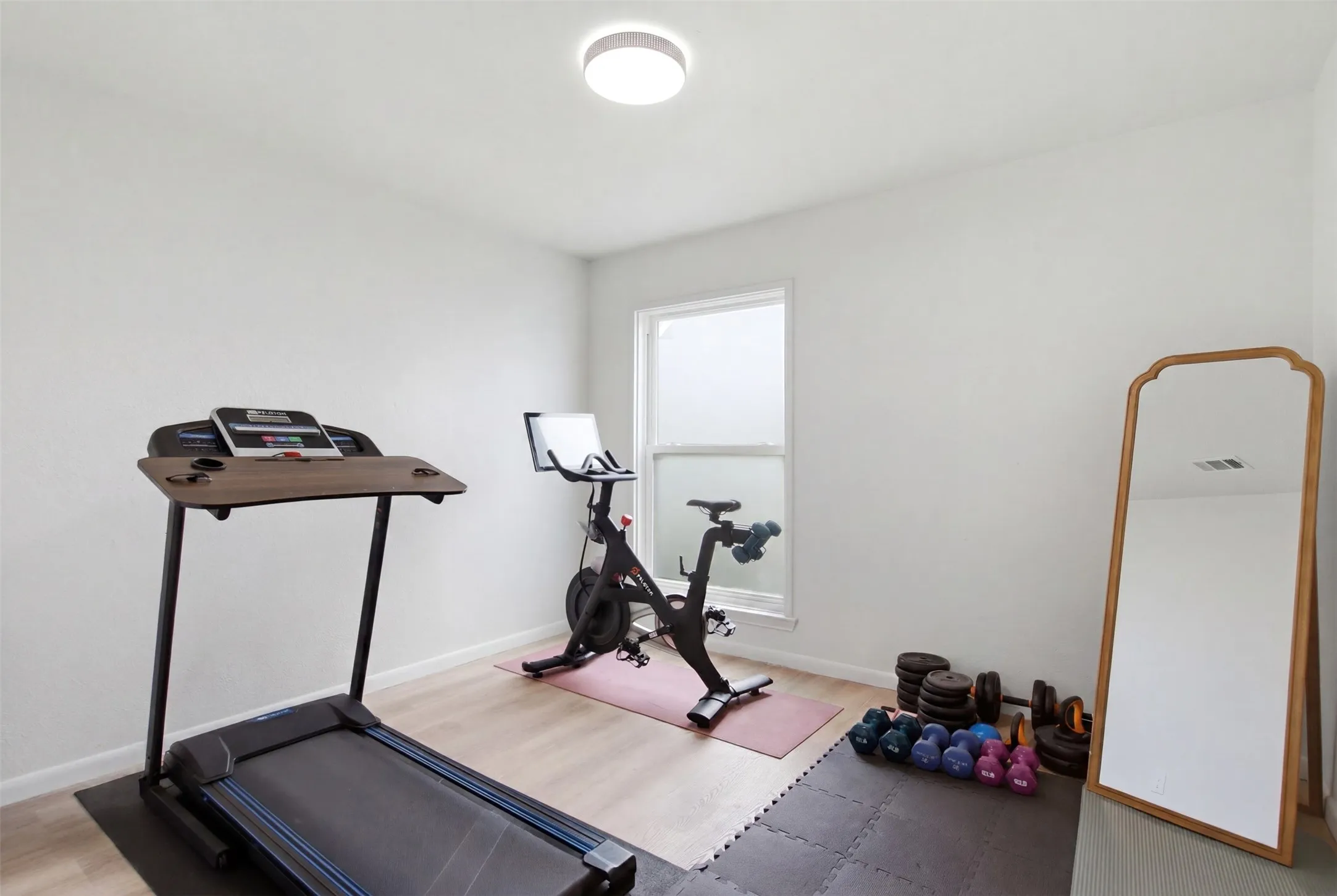 Versatile room featuring wood-finish flooring, a contemporary ceiling light fixture, and a window with privacy covering