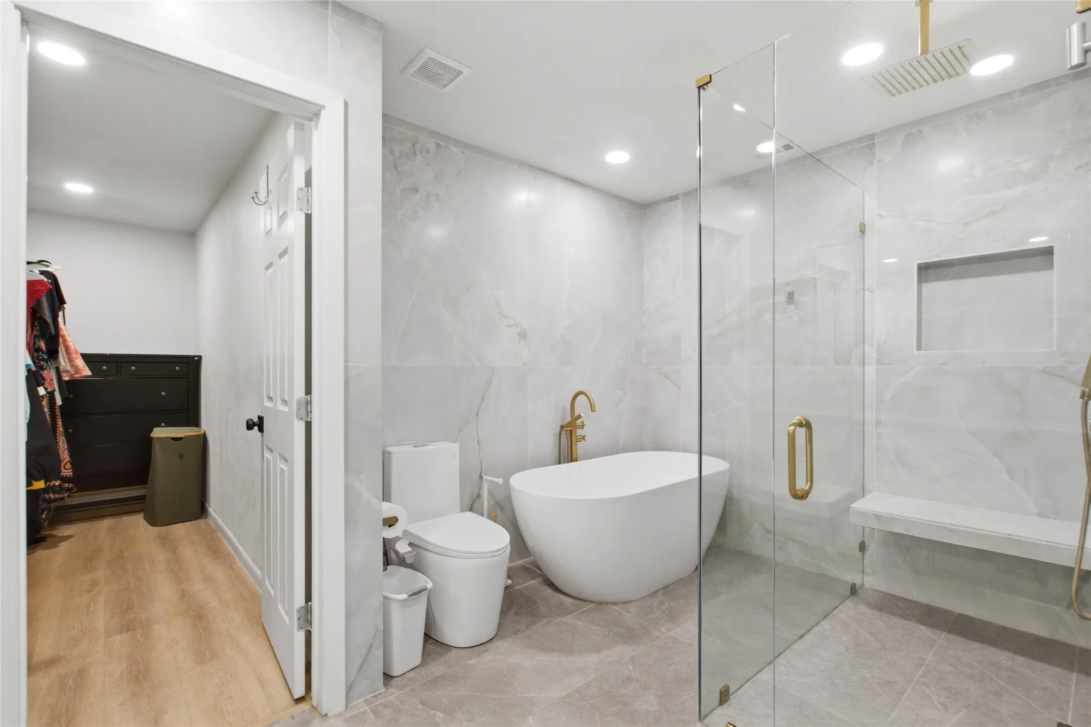Bathroom featuring a freestanding soaking tub, a frameless glass shower enclosure, a built-in shower bench, a recessed shower niche, and gold-finish fixtures