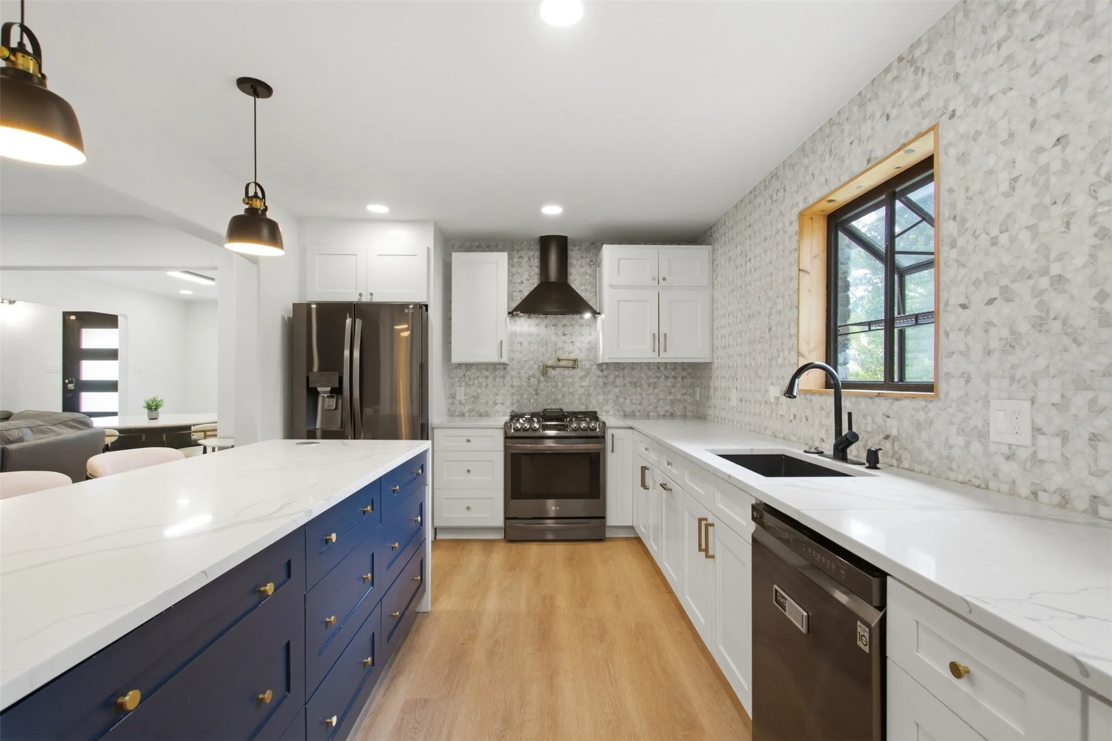 Modern kitchen featuring a large central island with a white countertop and blue cabinetry, white perimeter cabinetry with white countertops, stainless steel appliances, and a mosaic tile backsplash extending to the ceiling