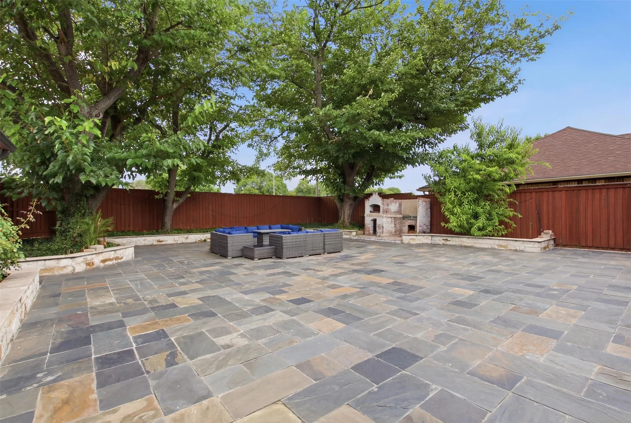 Expansive outdoor patio featuring flagstone paving, a built-in stone oven, stone retaining walls, and mature trees