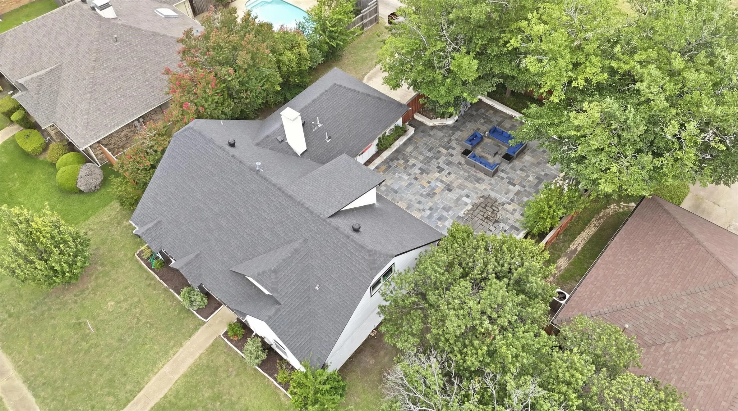 Aerial perspective highlighting the property's roofline, a private paved patio, and mature trees