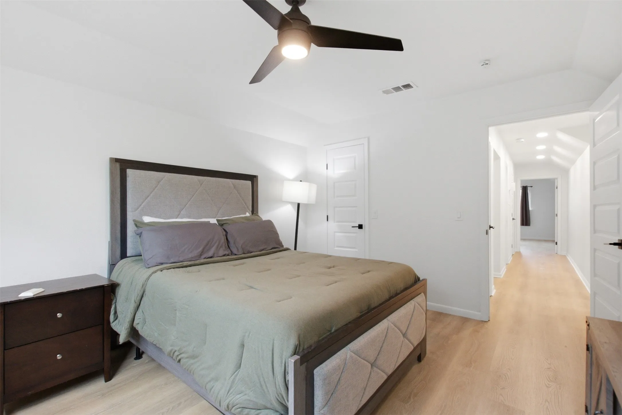 Bright interior room featuring light wood-finish flooring, a modern black ceiling fan with integrated lighting, and crisp white walls