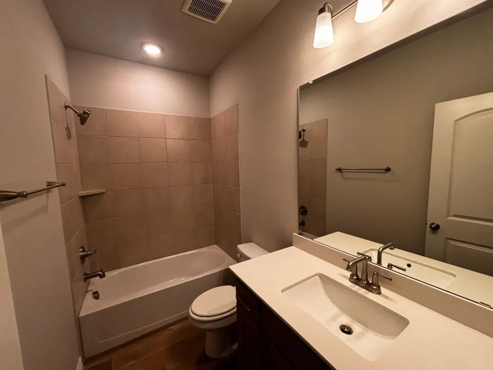 Integrated tub and shower with tile surround, wood-finish flooring, recessed lighting, and a vanity with a rectangular undermount sink
