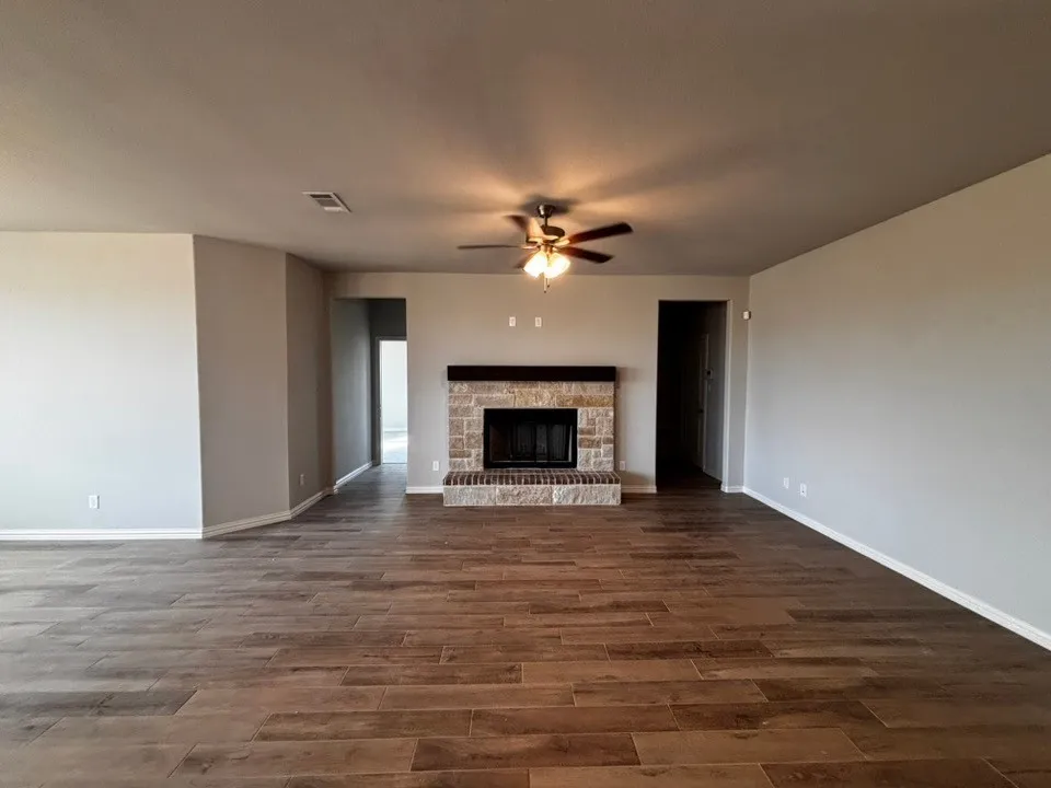 Spacious living area featuring wood-finish flooring, a stone fireplace with a dark wood mantel, and a ceiling fan with integrated lighting