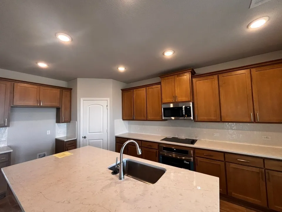 Kitchen featuring an expansive island with an undermount stainless steel sink, recessed lighting, wood-finish cabinetry, and stainless steel appliances