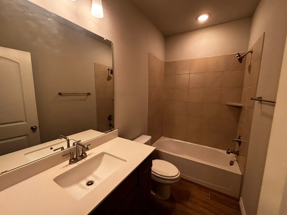 Bathroom featuring a single vanity with an integrated sink, brushed nickel faucet, a large wall-mounted mirror, and wood-finish flooring
