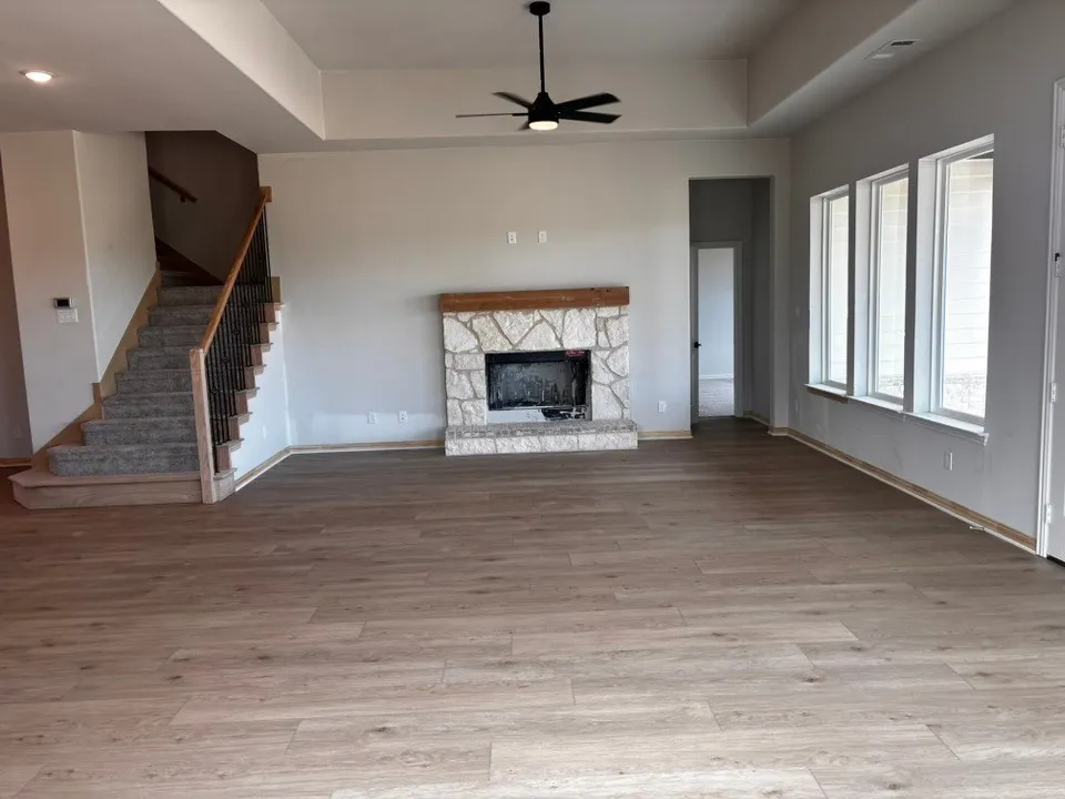 Wood-finish flooring, stone-faced fireplace with wood mantel, multiple windows, and a staircase with wood newel posts and iron balusters