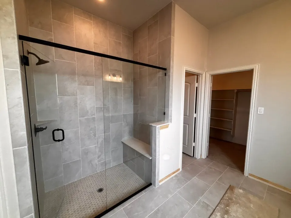 Walk-in shower with tiled walls and floor, frameless glass enclosure, built-in bench, and black fixtures