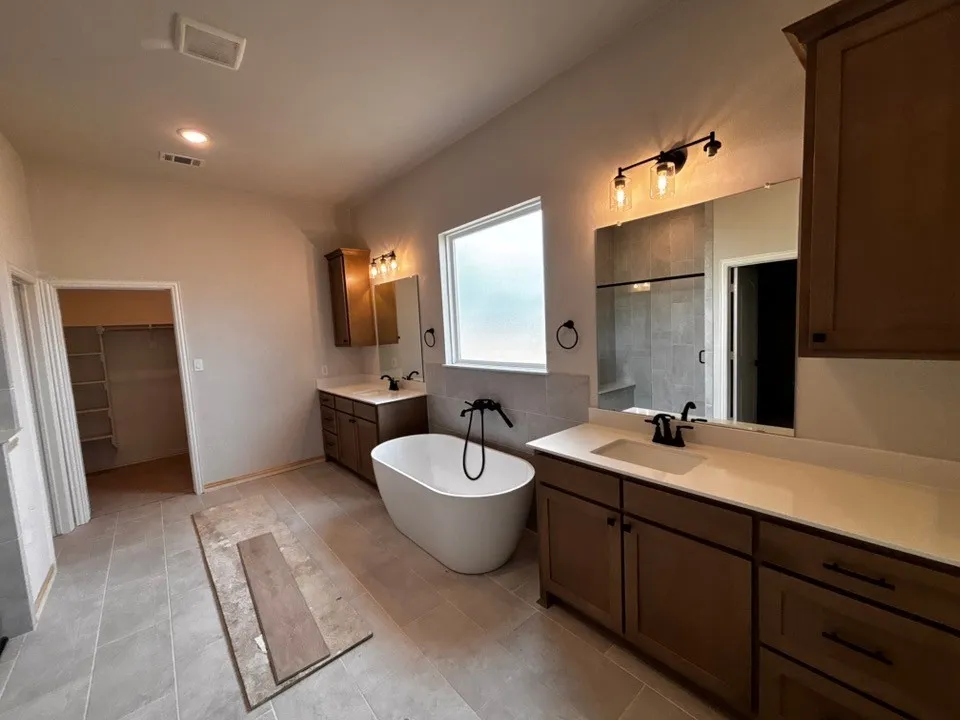 Freestanding soaking tub, wood-finish vanities with light countertops, dual rectangular undermount sinks, and tile flooring