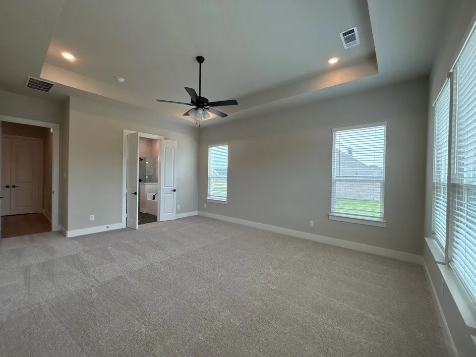 Expansive carpeted room featuring a tray ceiling with recessed lighting, a ceiling fan, and multiple windows with blinds