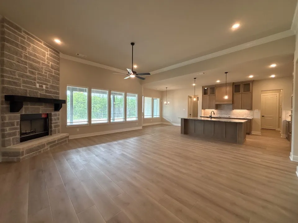 Open-concept living area featuring a stone-clad fireplace, wood-finish flooring, and a kitchen island with pendant lighting