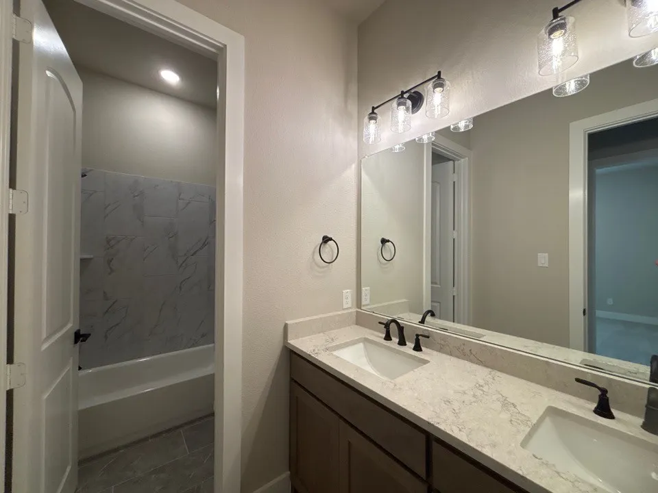 Dual vanity with light-toned countertop and integrated sinks, matte black fixtures, and wood-finish cabinetry