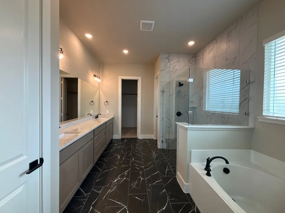 Dual vanity with undermount sinks and quartz countertops, walk-in shower with glass enclosure, freestanding soaking tub with matte black fixtures, recessed lighting, and large format tile flooring