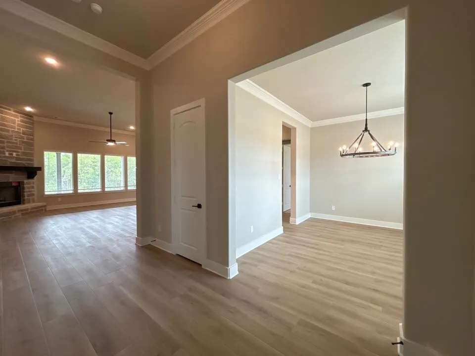Wood-finish flooring throughout, crown molding, stone-clad fireplace with mantel, recessed lighting, and a contemporary chandelier