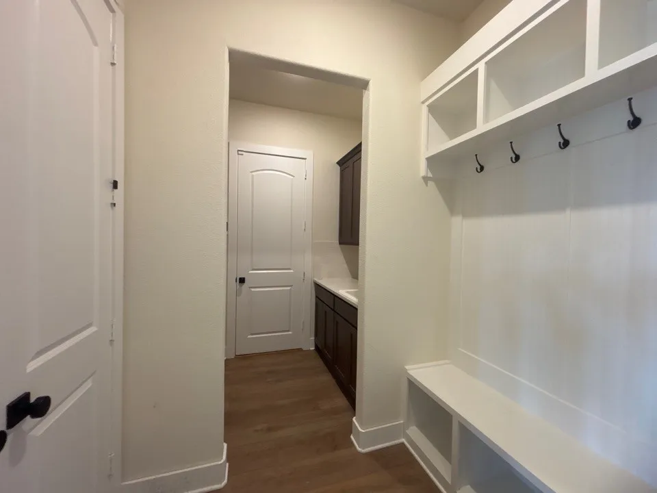 Mudroom featuring abundant built-in storage with open shelving and hooks, wood-finish flooring, and a convenient sink with dark cabinetry for easy cleanup and organization