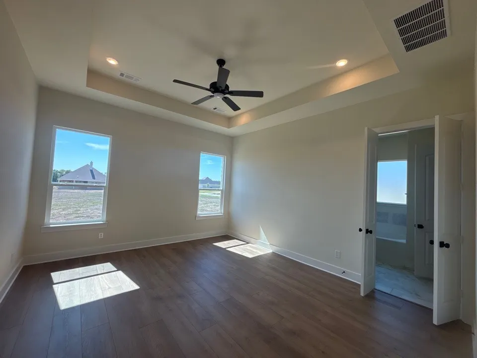 Spacious room featuring tray ceiling with recessed lighting, ceiling fan, wood-finish flooring, and two windows