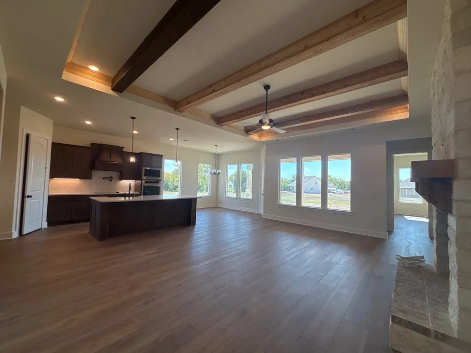 Open-concept living space featuring wood-finish flooring, a tray ceiling with exposed wood beams, and multiple windows