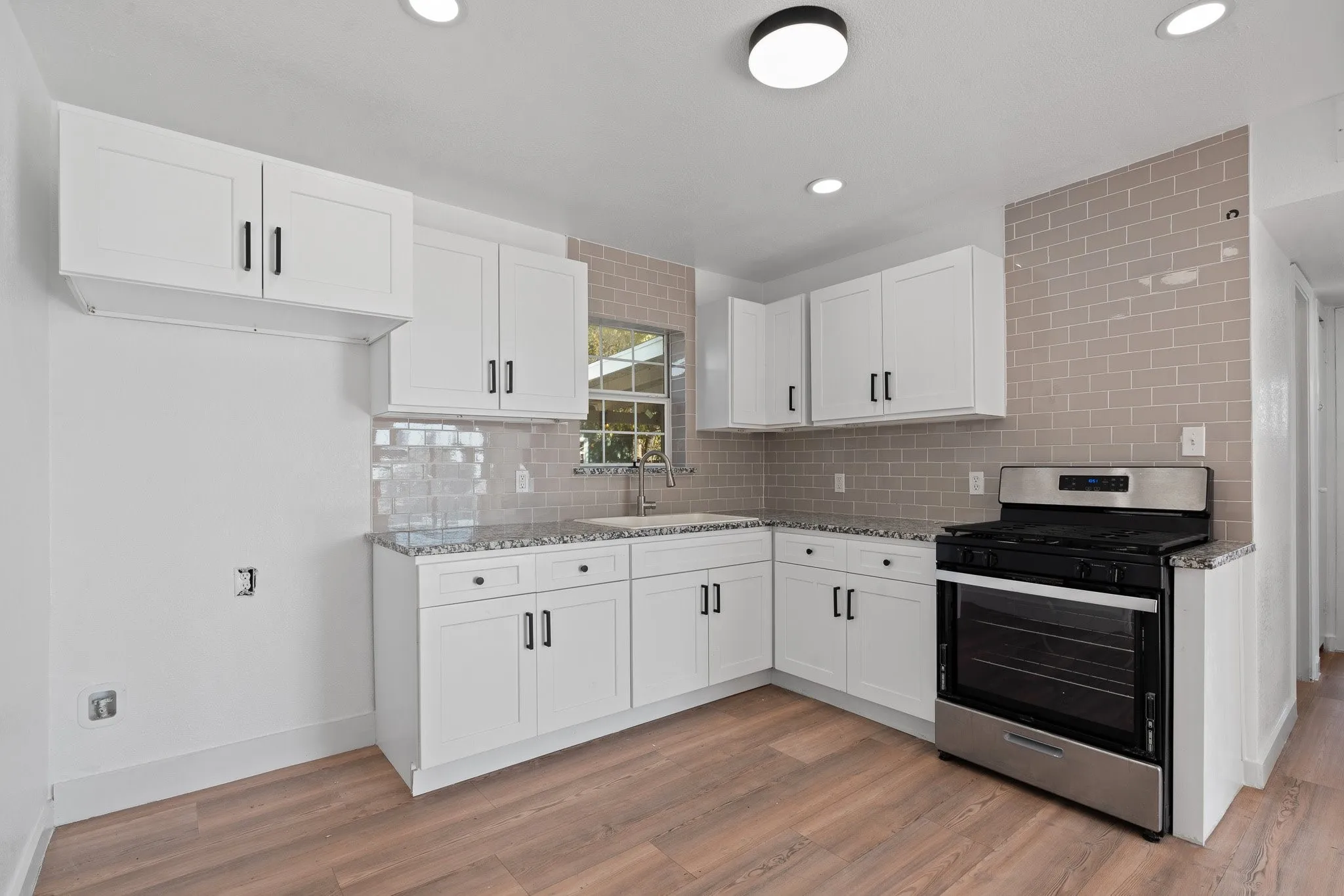 Kitchen featuring wood-finish flooring, white cabinetry with black hardware, light-toned subway tile backsplash, and granite countertops