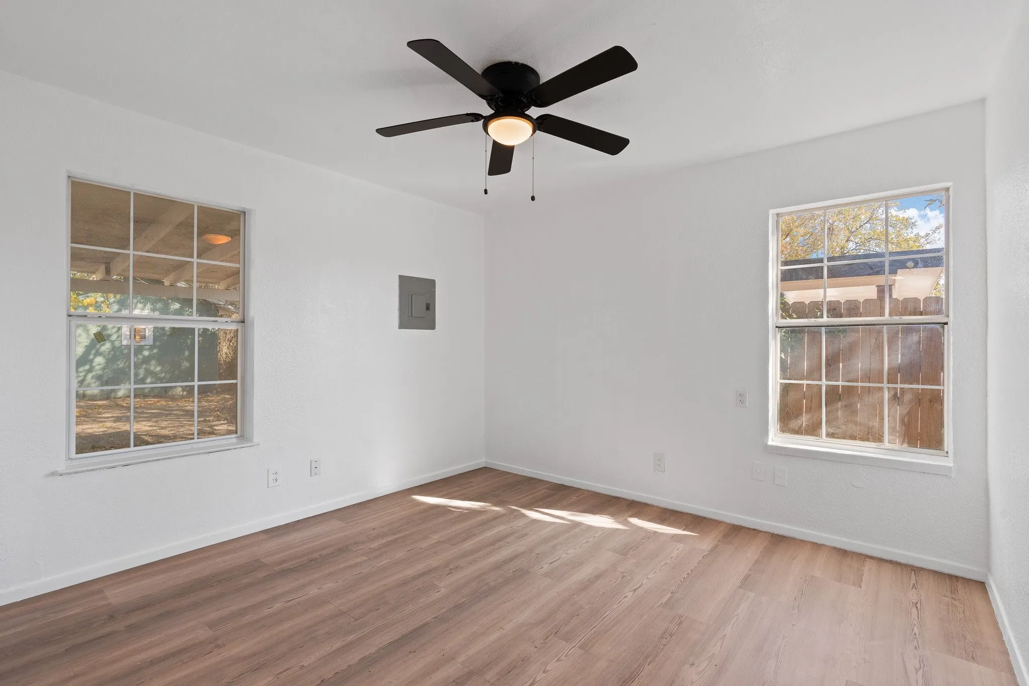 Bright interior space featuring wood-finish flooring, white walls, two windows, and a ceiling fan with integrated lighting
