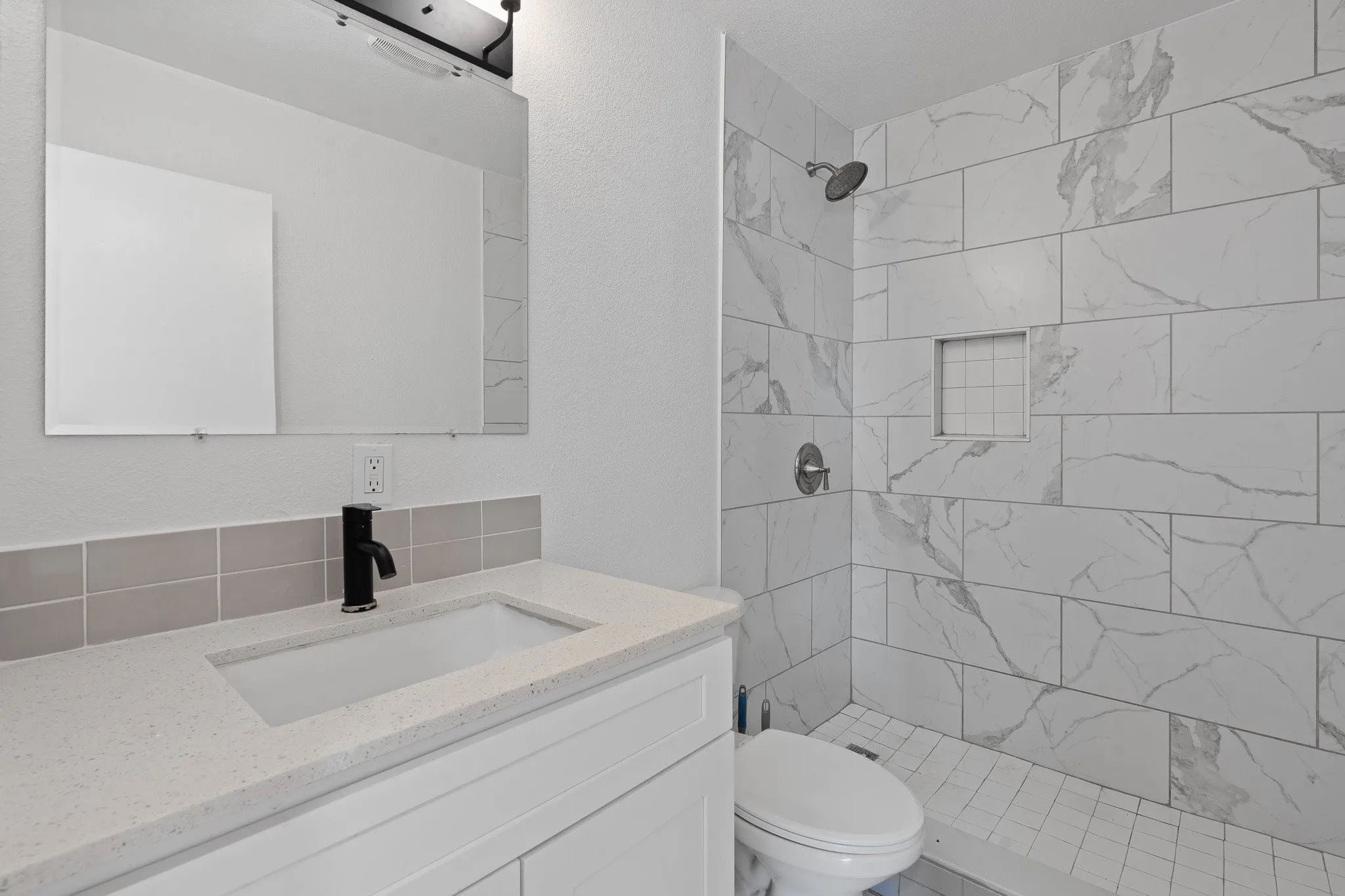 White subway tile shower surround with integrated niche, sleek black faucet, and a contemporary vanity with a white rectangular sink