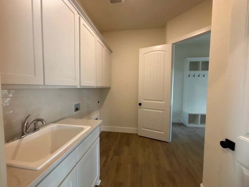 White shaker cabinetry, utility sink with chrome faucet, wood-finish flooring, and a built-in mudroom bench with hooks and cubbies