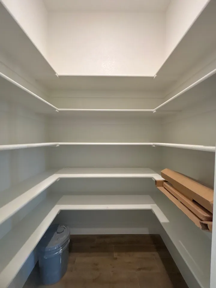 Walk-in pantry featuring white shelving and wood-finish flooring
