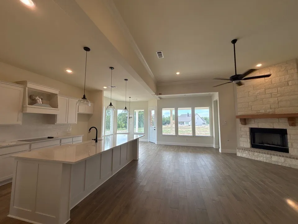 Open-concept layout featuring wood-finish flooring, a stone-surround fireplace with a wood mantel, and a kitchen island with pendant lighting