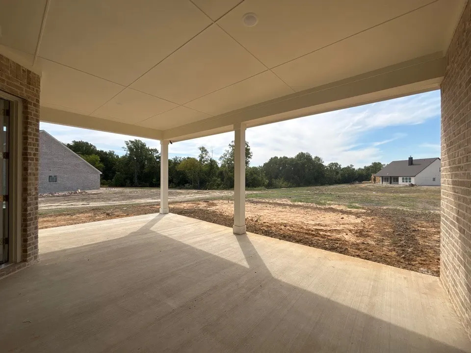 Covered patio with a concrete surface, supported by white columns, featuring a light-colored brick exterior
