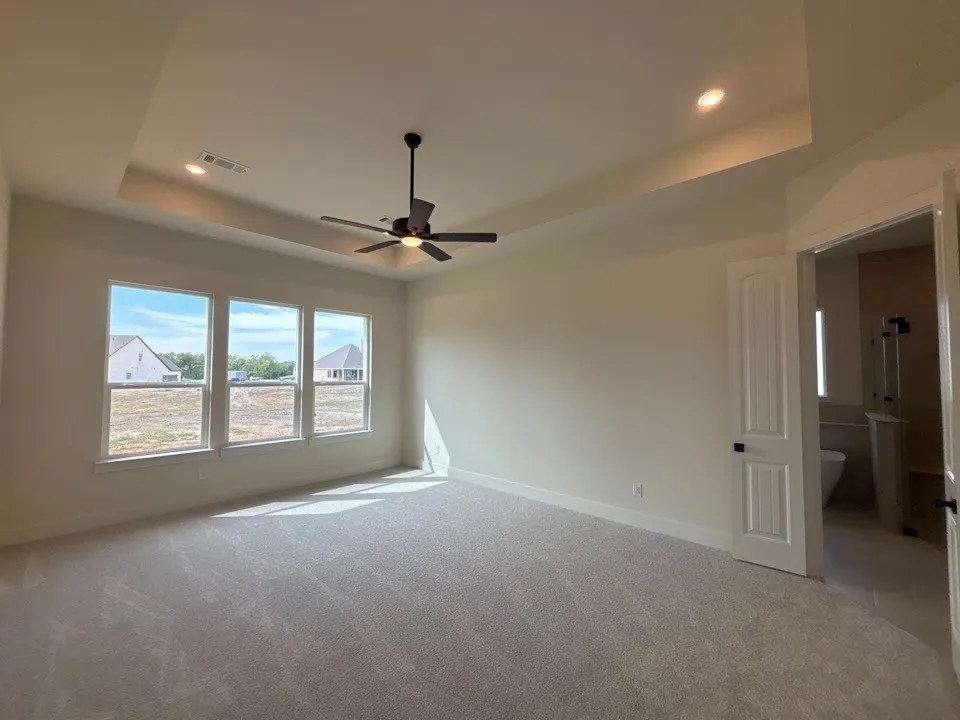 Expansive room featuring a tray ceiling, three large windows, a ceiling fan with integrated lighting, recessed lighting, and light-colored carpeting