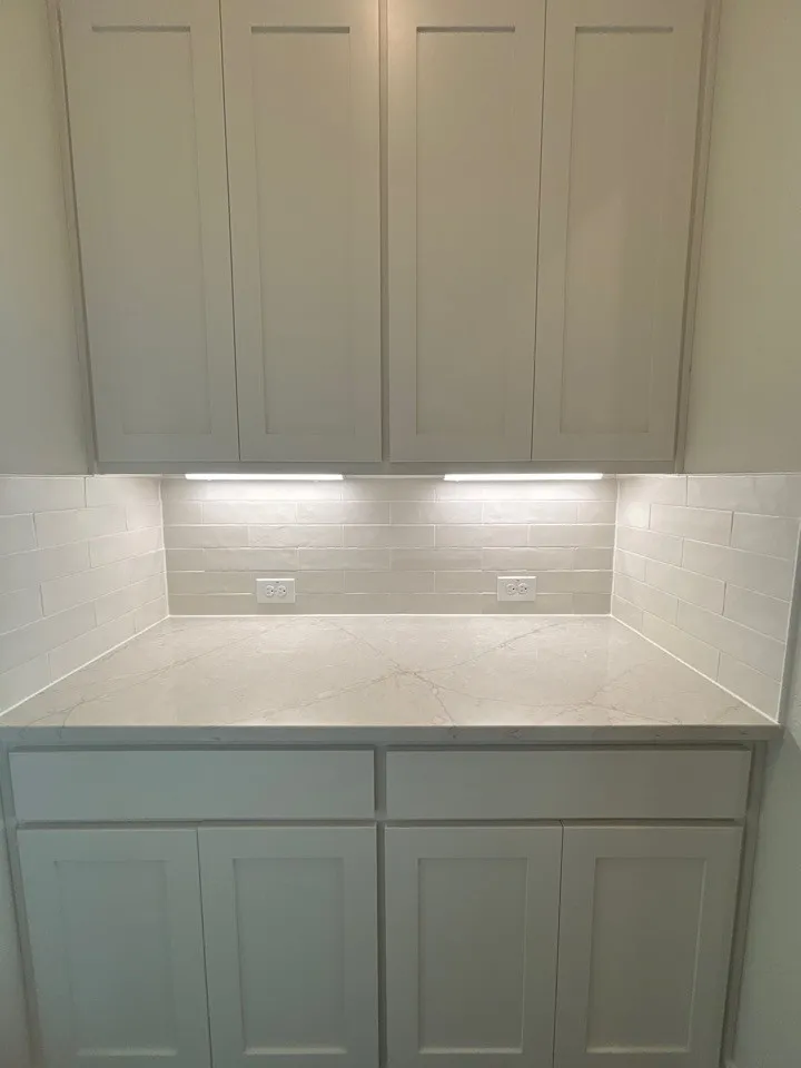Shaker-style cabinetry, undermount lighting, subway tile backsplash, and a light-toned countertop