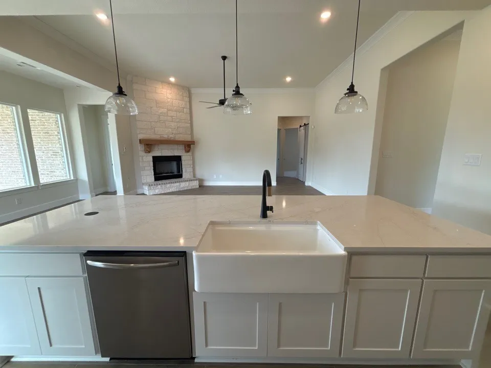 Central kitchen island featuring quartz countertops, an undermount farmhouse sink with a gooseneck faucet, white shaker-style cabinetry, and a stainless steel dishwasher