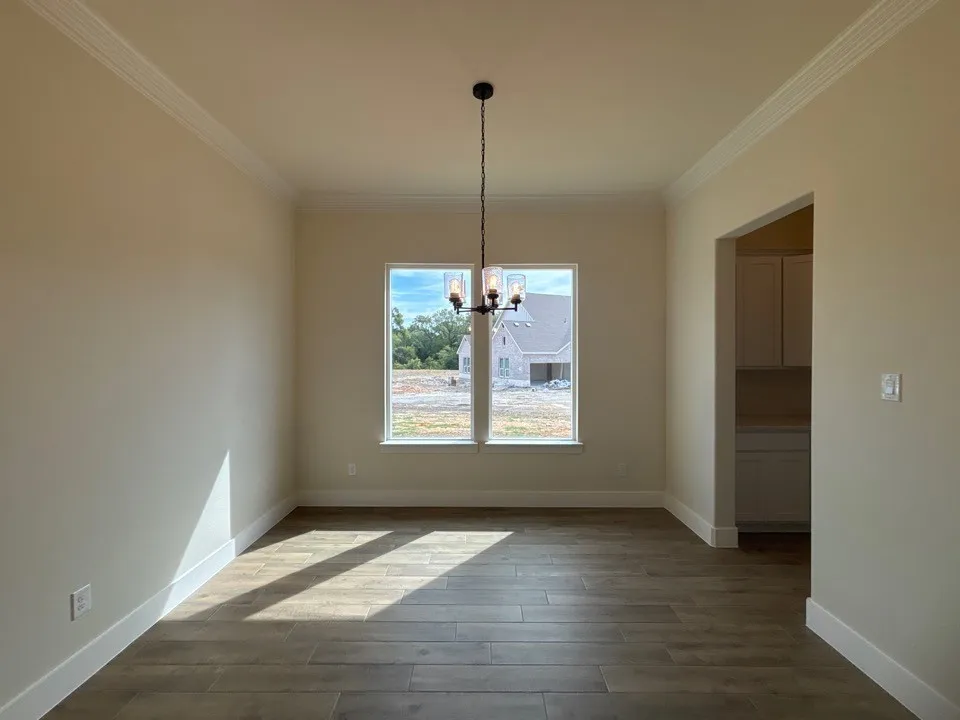 Wood-finish flooring, crown molding, and a modern chandelier