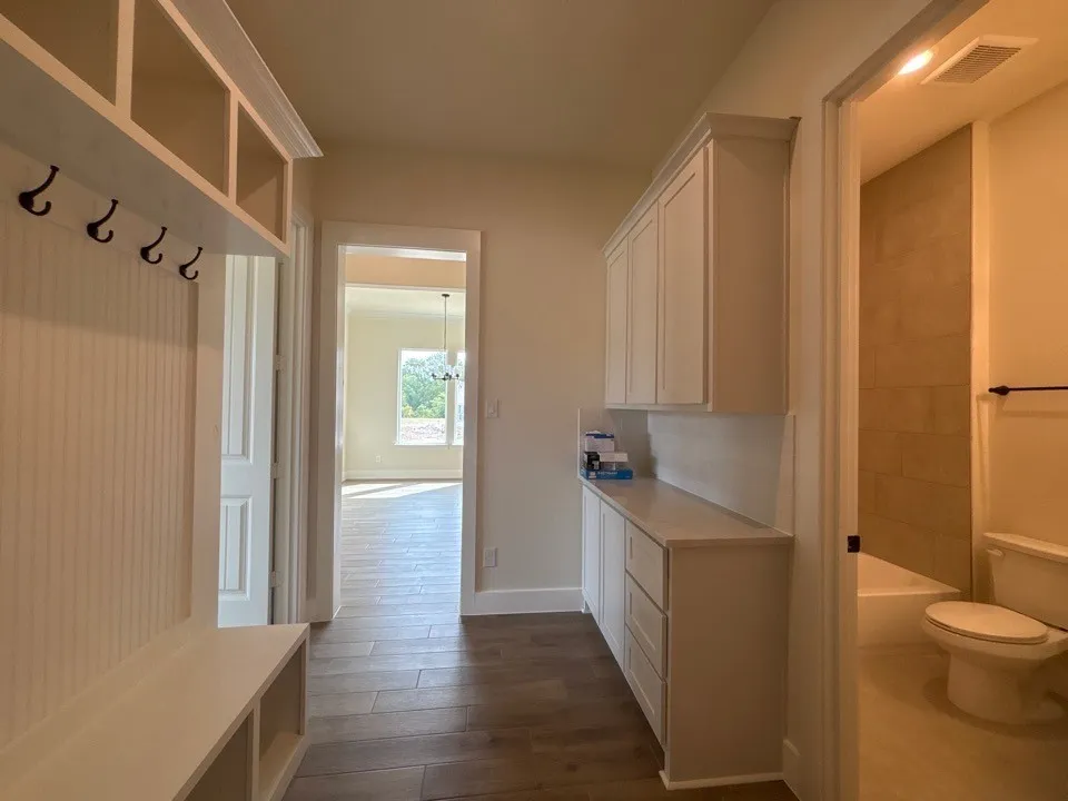 Mudroom with built-in bench and storage, wood-finish flooring, white cabinetry with countertop, and a full bathroom featuring a tub