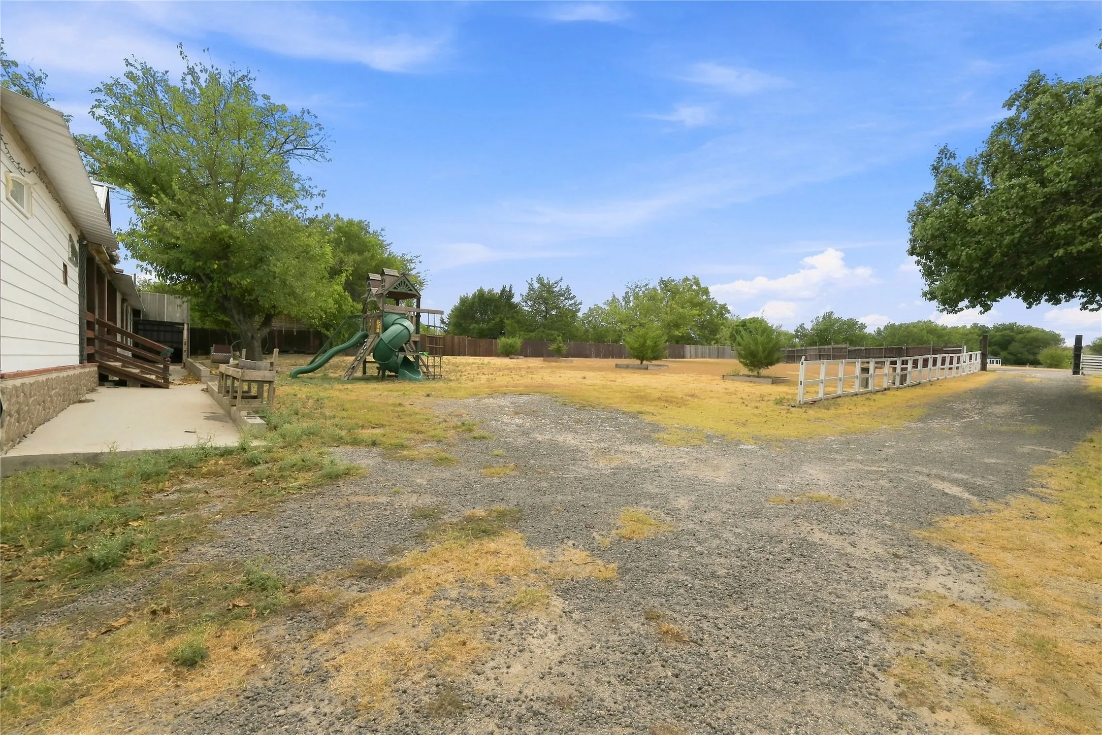 Expansive outdoor area featuring a gravel path, white fencing, and mature trees