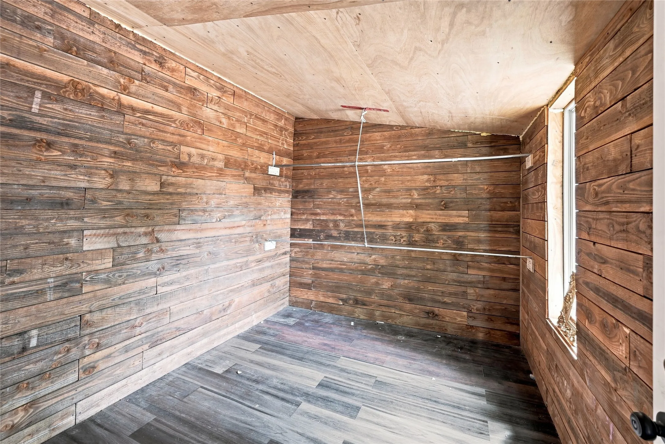 Wood-paneled walls with a natural finish, wood-finish flooring, and a single window